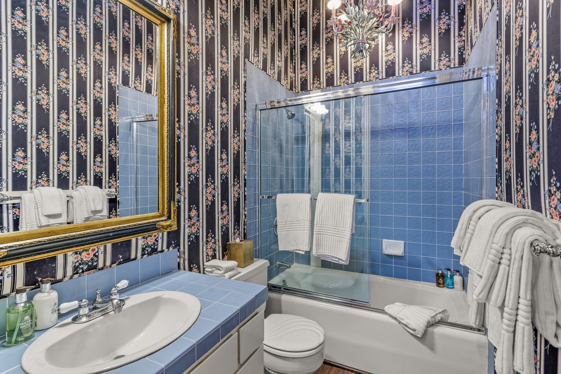 Bathroom with blue tile and wallpaper with floral stripes.