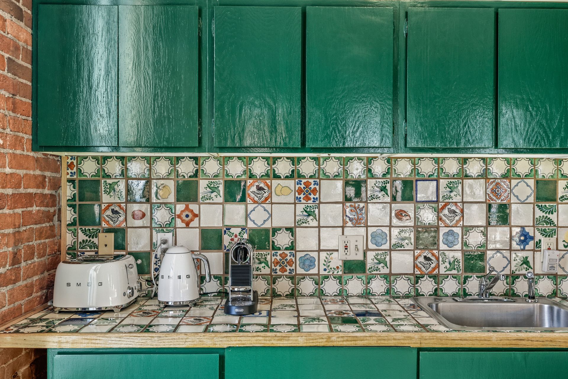 Green cabinets, patterned tile backsplash and countertop, brick wall, kitchen appliances.