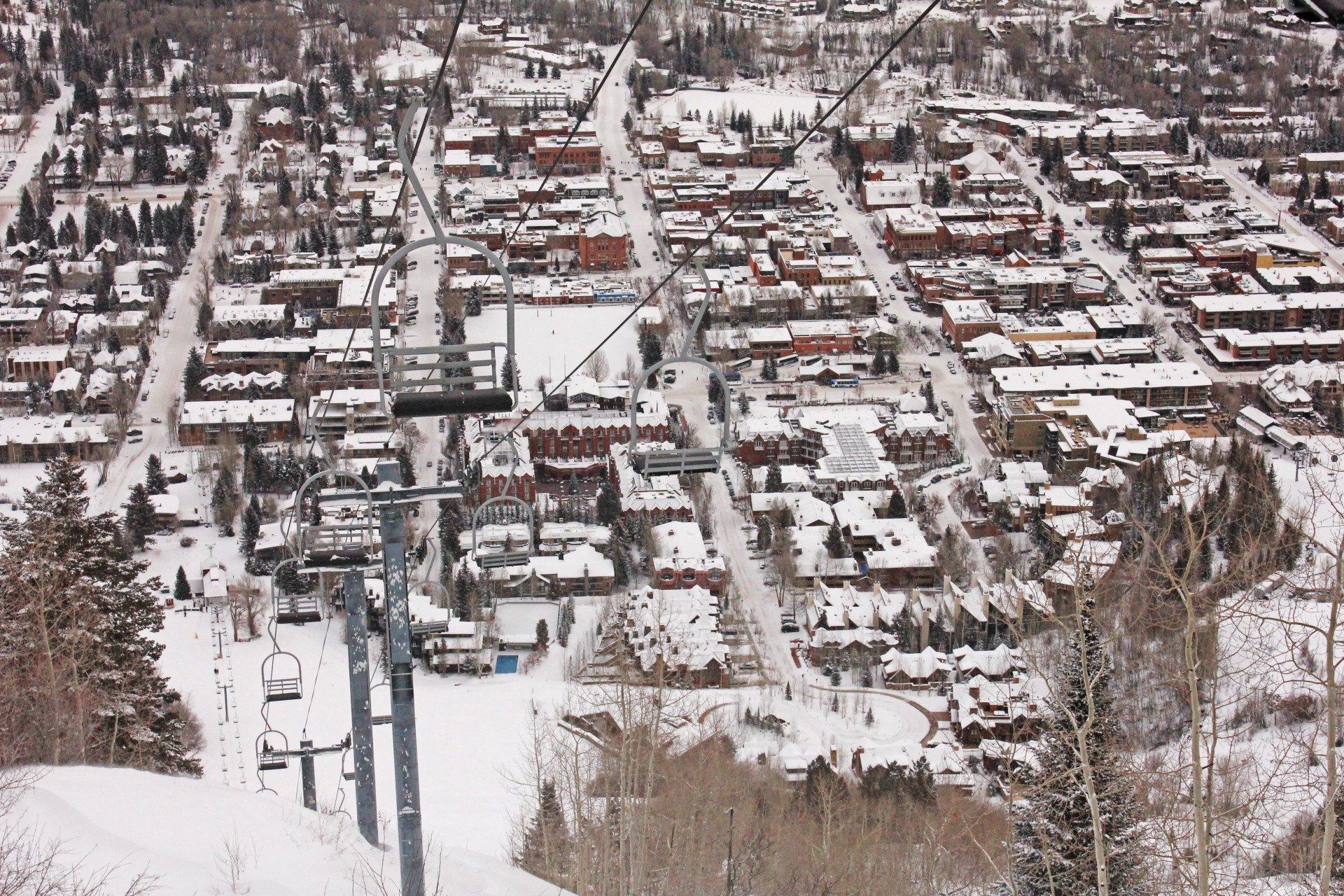 Aerial view of a snow-covered town, with ski lift in foreground. Buildings are mostly brown and white.