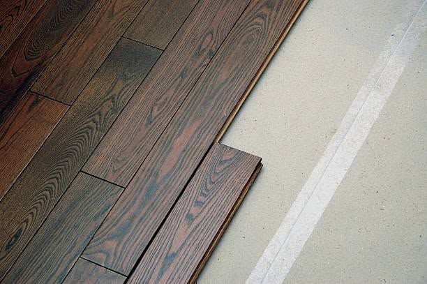 Partial wood flooring installation beside beige carpet with white transition strip