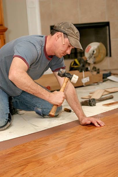 Worker installing a wood floor with a hammer and chisel in a home interior