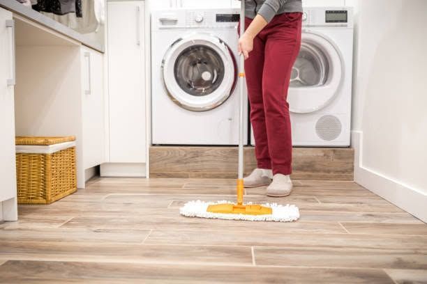 Person mopping a laundry room floor beside a washer and dryer