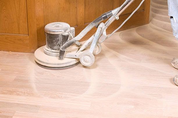 Floor sander polishing a wooden floor beside a cabinet