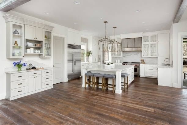 Bright white kitchen with island, stainless fridge, and dark hardwood floors