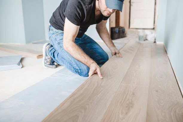 Worker installing light wood flooring in a bright room