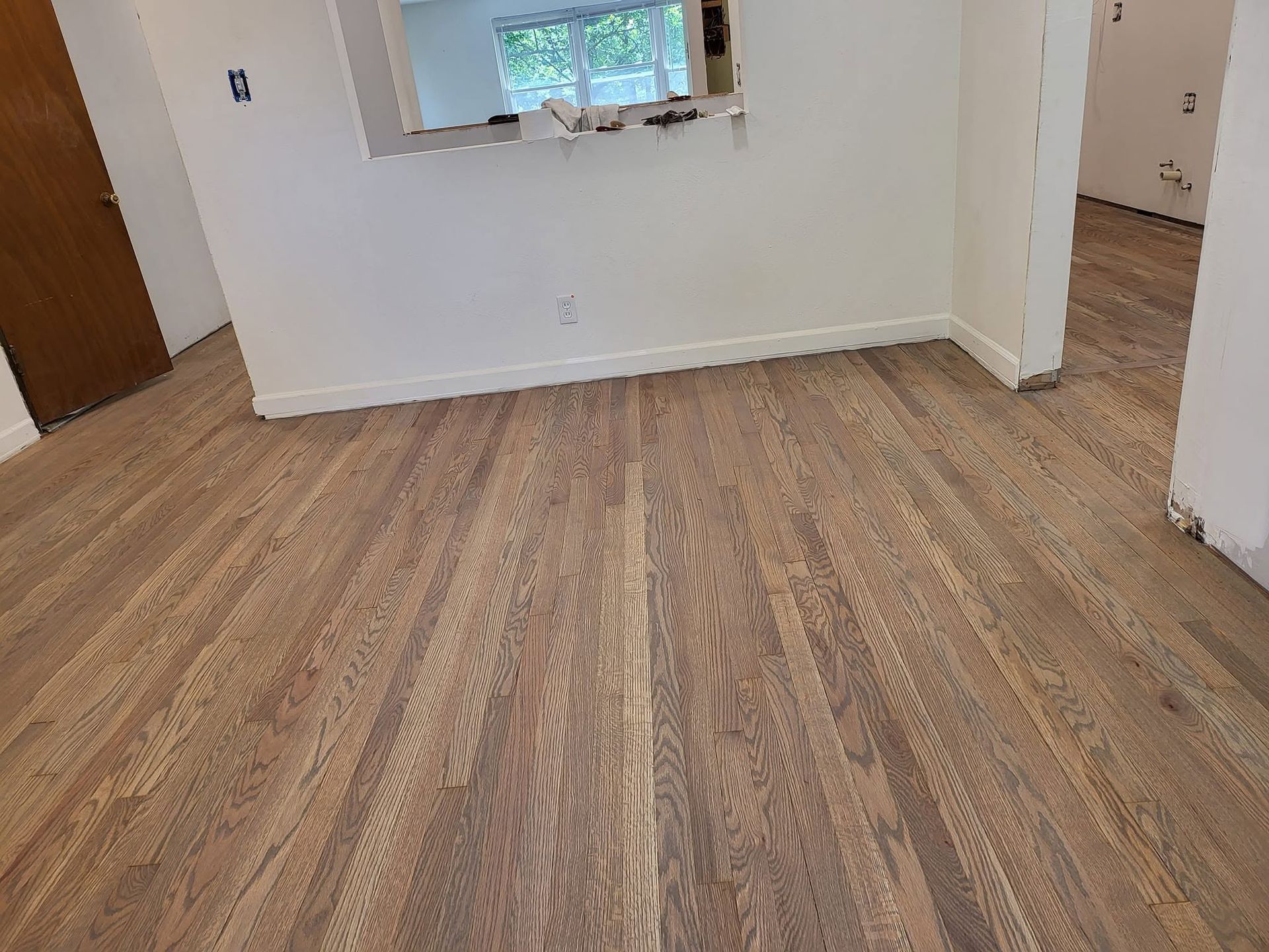 Empty room with light wood flooring, white walls, and a small window near a doorway.