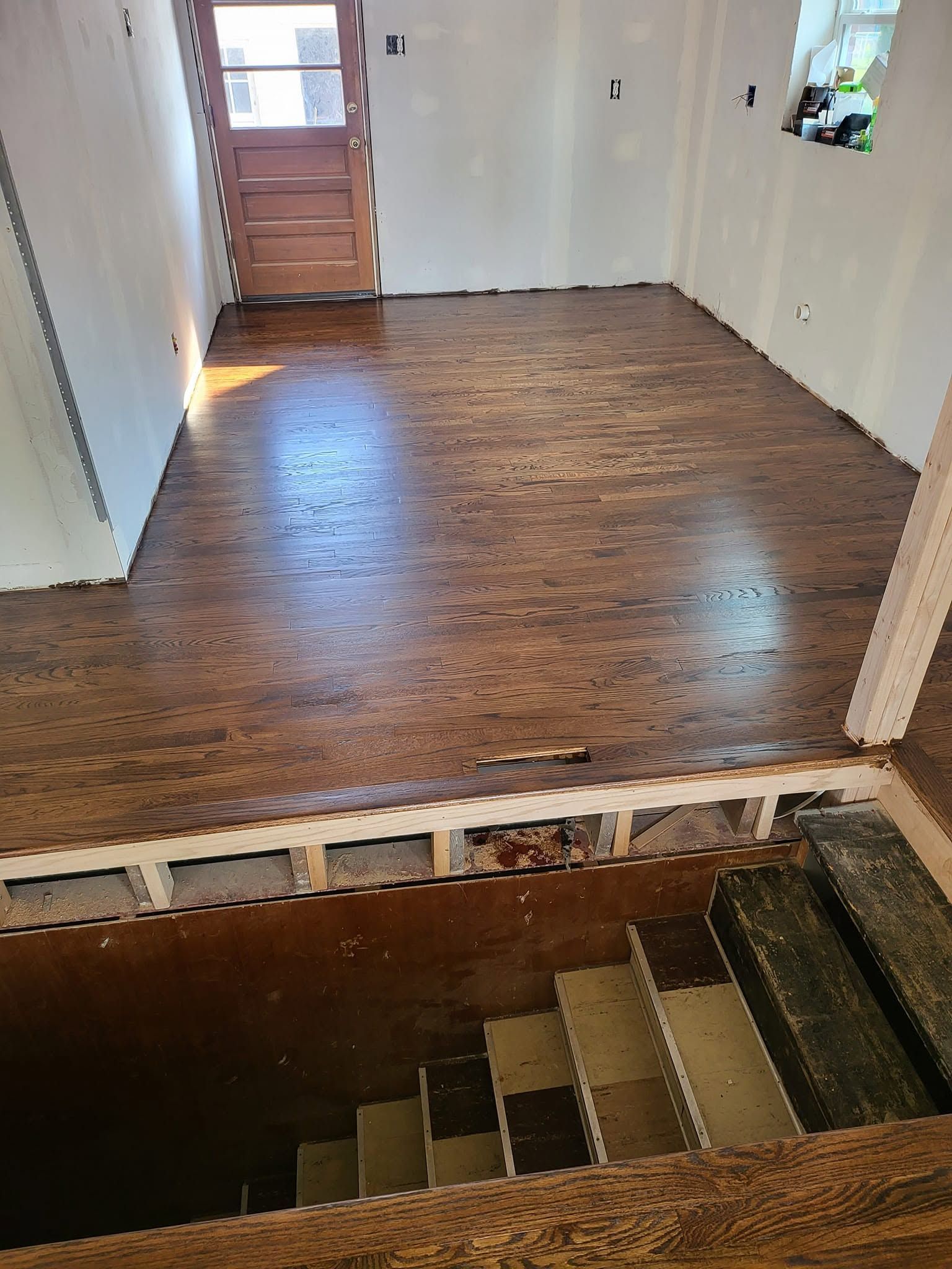 View from top of staircase into empty room with wood floor and white walls