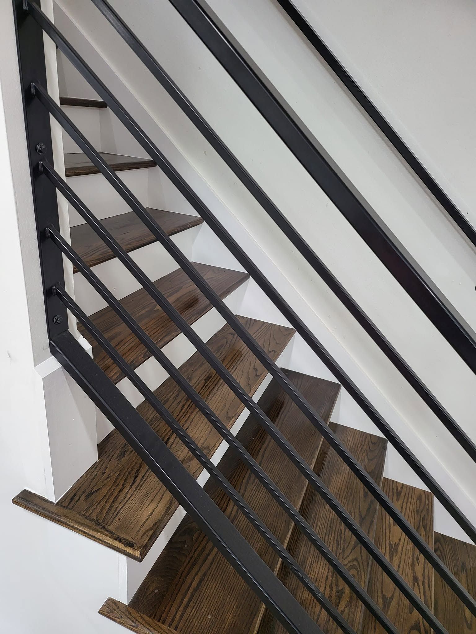 Steep indoor staircase with brown carpet and black metal railings.