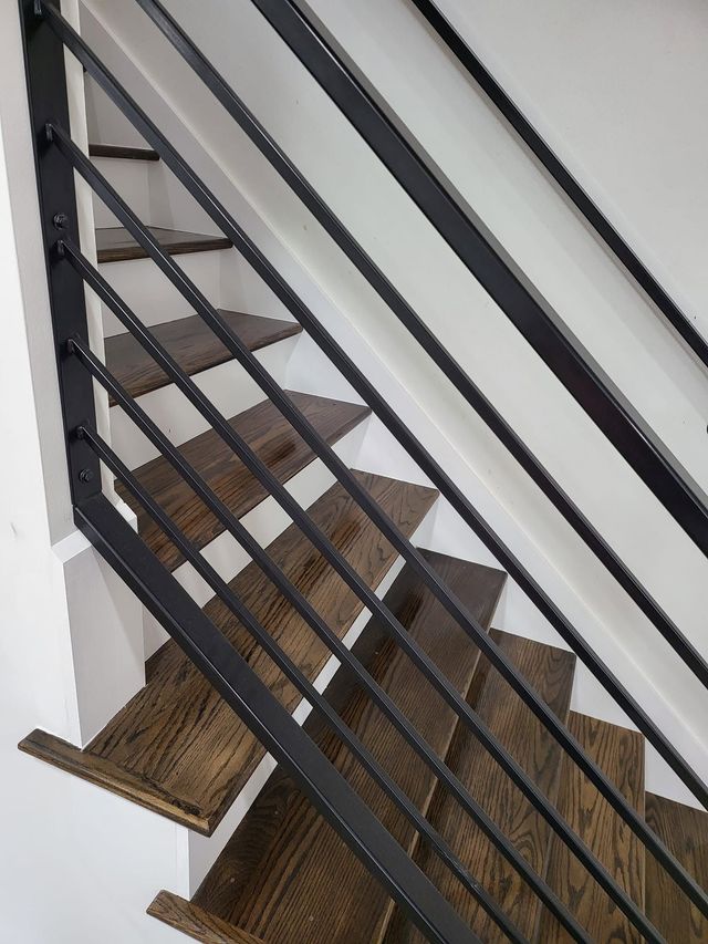 Indoor staircase with brown carpeted steps and black metal railing on the left