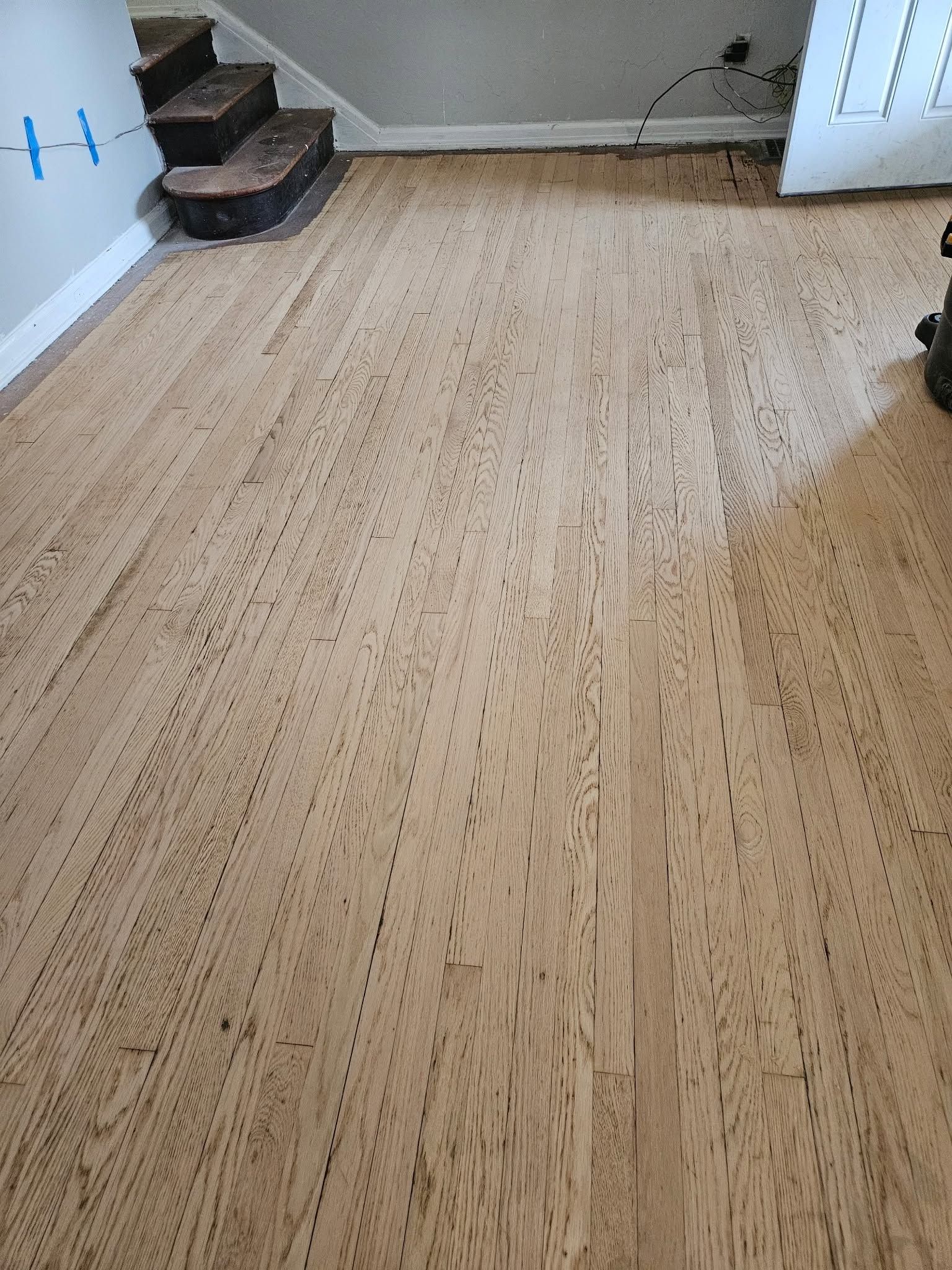 Empty room with wood floor, small steps on the left, and an open white door on the right.