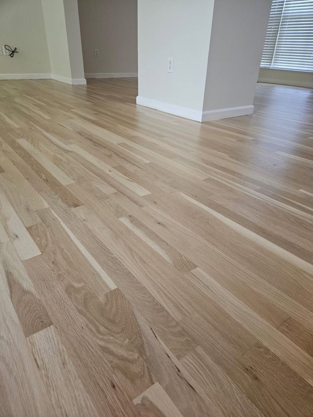 Empty room with light wood flooring and white walls near a hallway opening