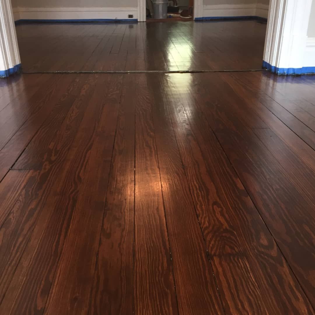 Glossy dark wood floor in a hallway with white doorways and blue painter’s tape along the baseboards