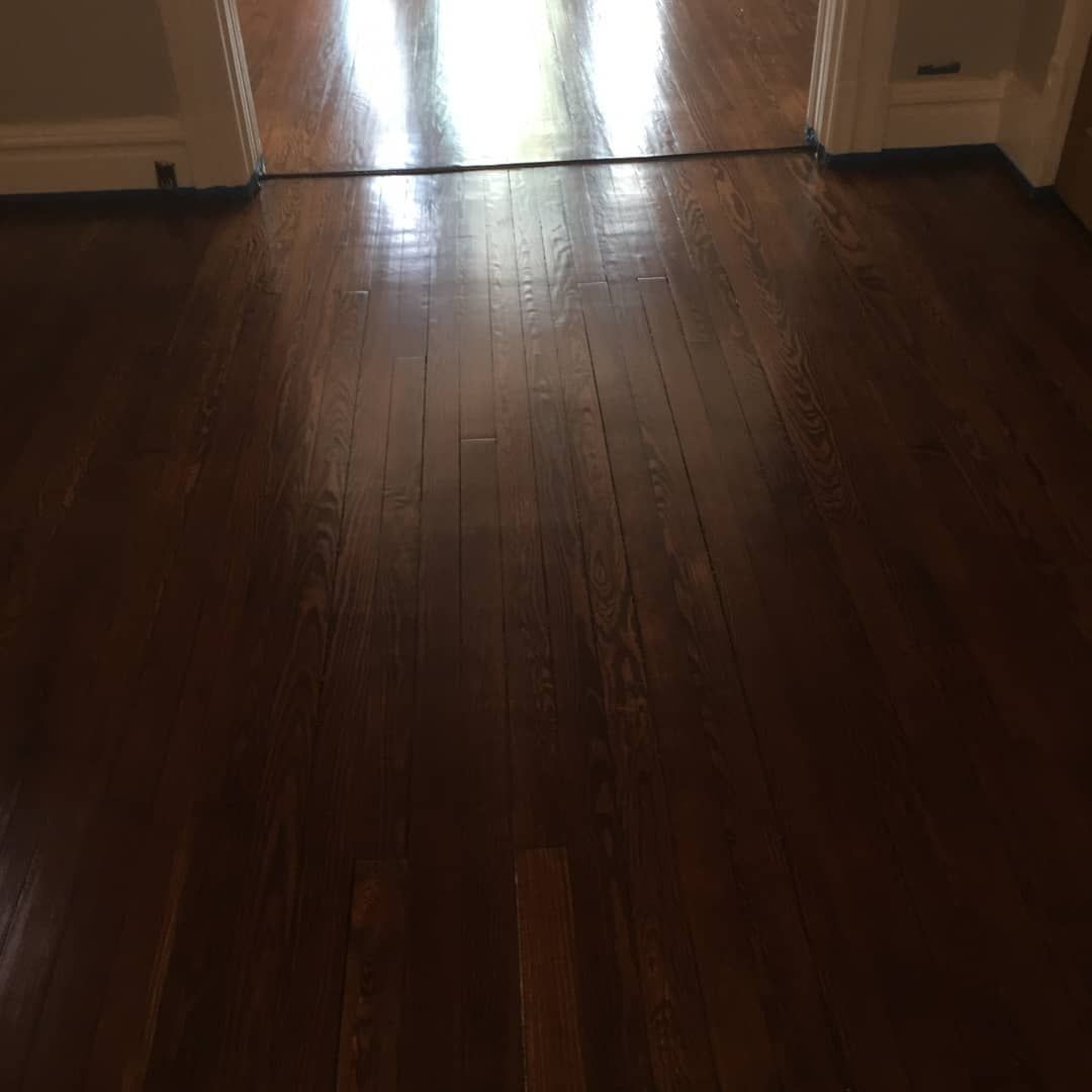 Dim hallway with dark wooden floor and bright light reflecting from a doorway ahead