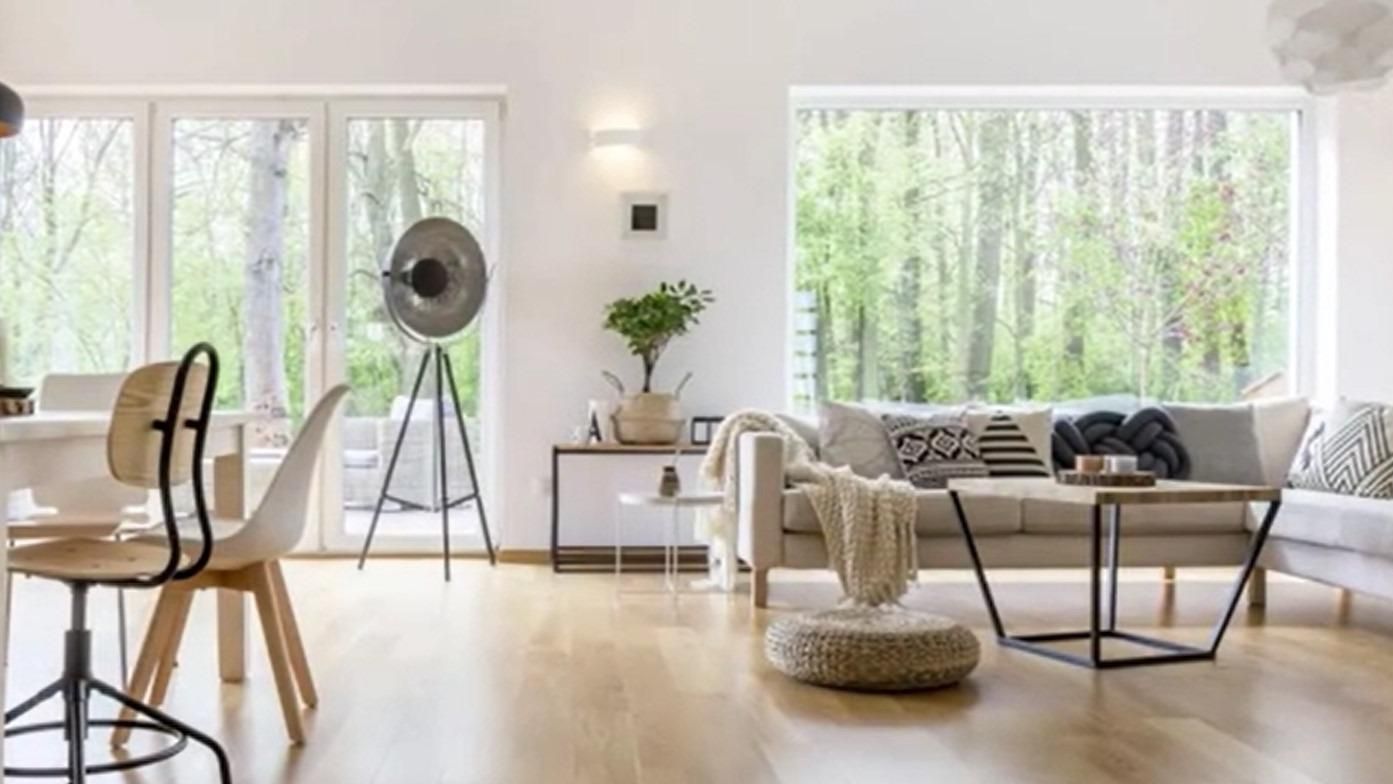 Bright modern living room with large windows, white furniture, a tripod lamp, and a woven chair.