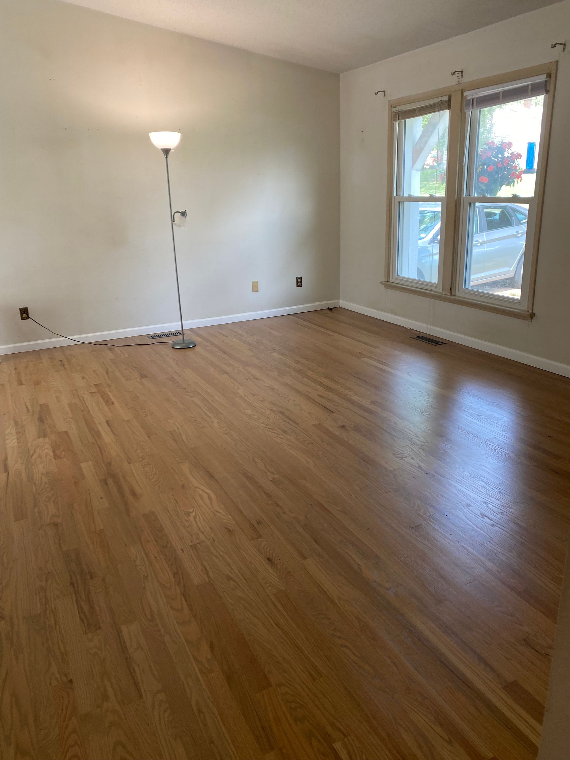 Empty living room with hardwood floors, beige walls, floor lamp, and French doors opening to a balcony.