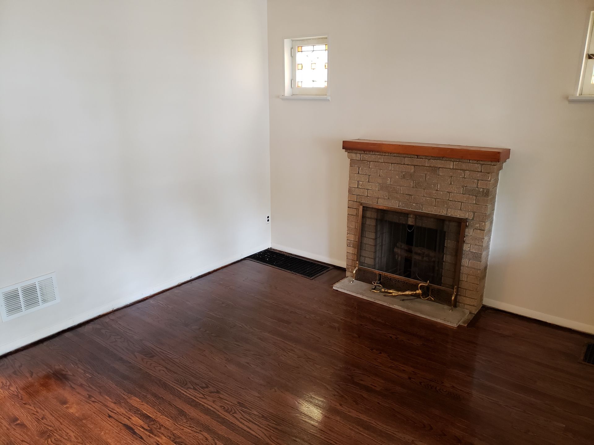 Empty room with dark hardwood floors, white walls, and a stone fireplace.