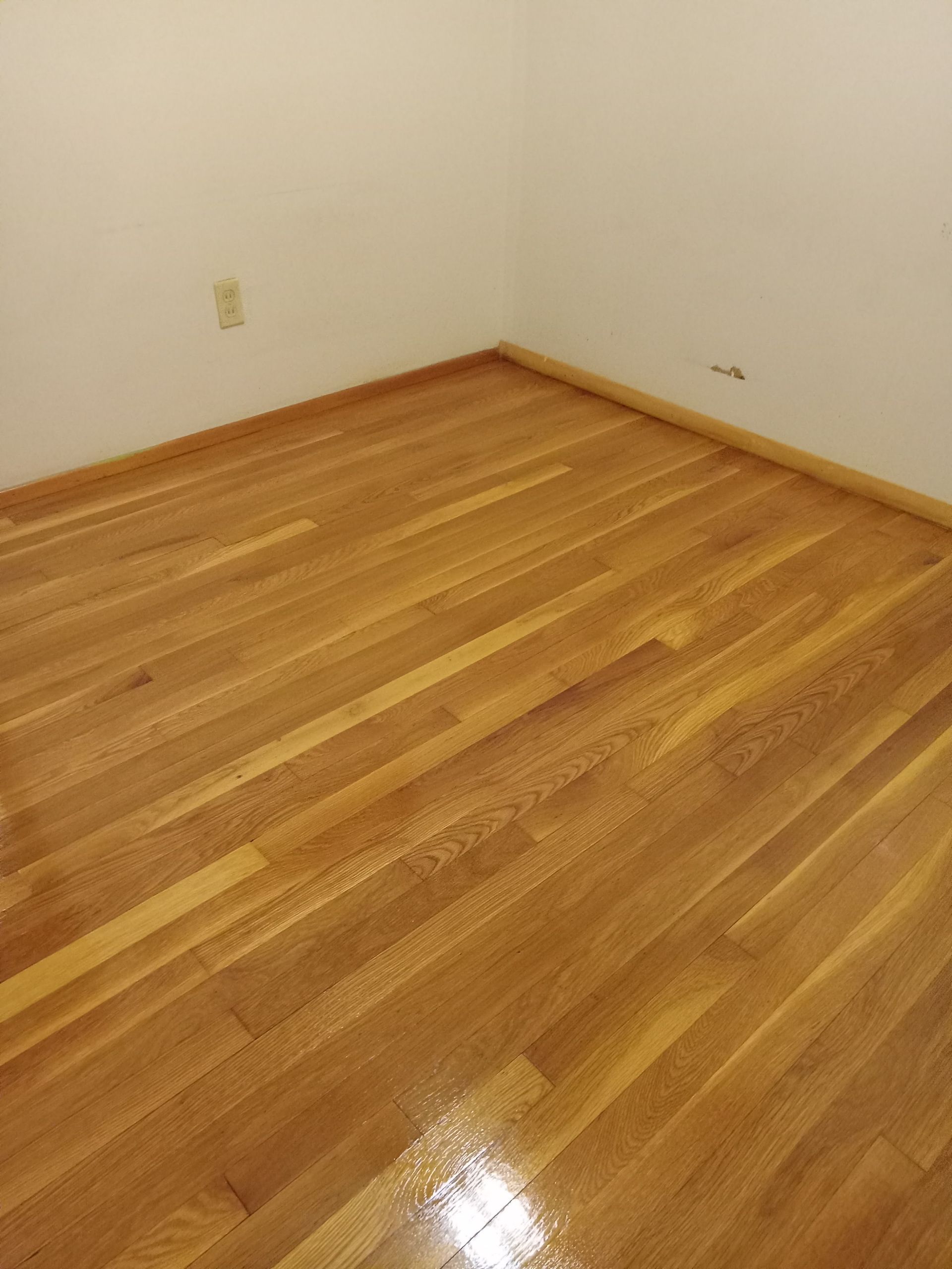 Empty room with hardwood floor and white walls, viewed from the corner.
