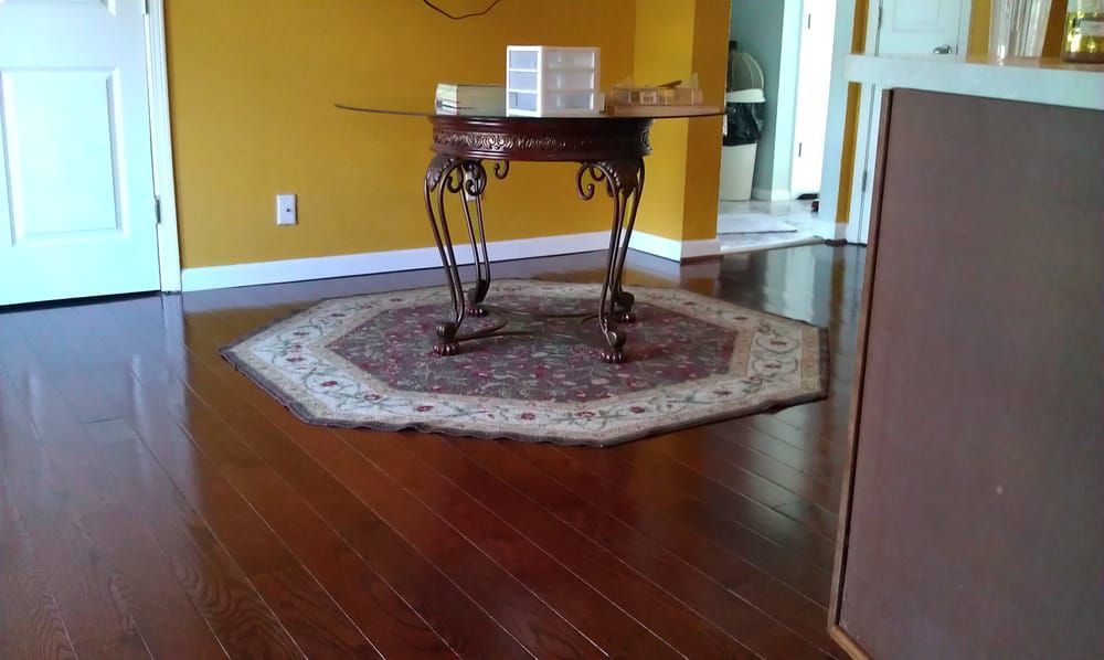 Empty living room with glossy wooden floor, ornate table on a patterned rug, and white doors.