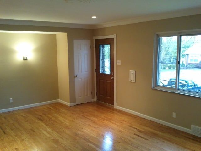 Empty living room with hardwood floors, beige walls, a front door, and a large window.