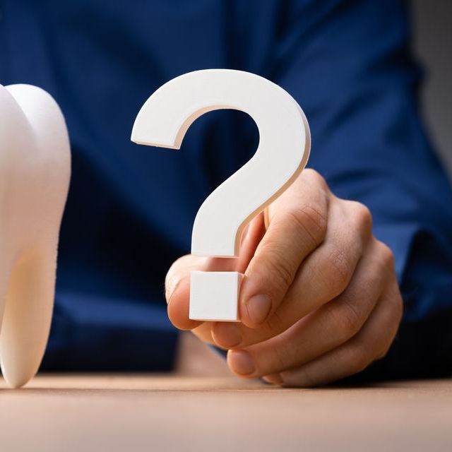 A person is holding a question mark in front of a piggy bank