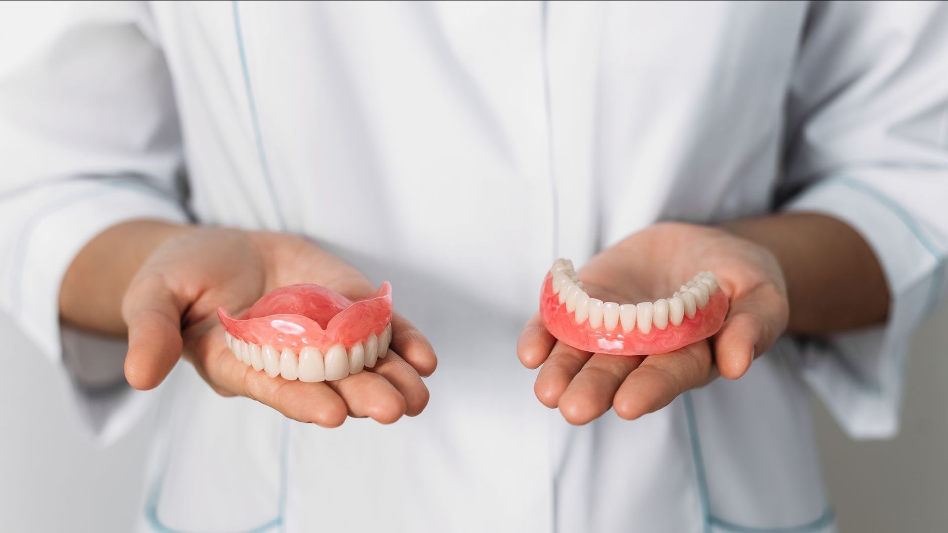 Un dentiste tient deux prothèses dentaires dans ses mains.