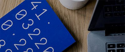 Un livre bleu est posé sur une table en bois à côté d'un ordinateur portable et d'une tasse de café.