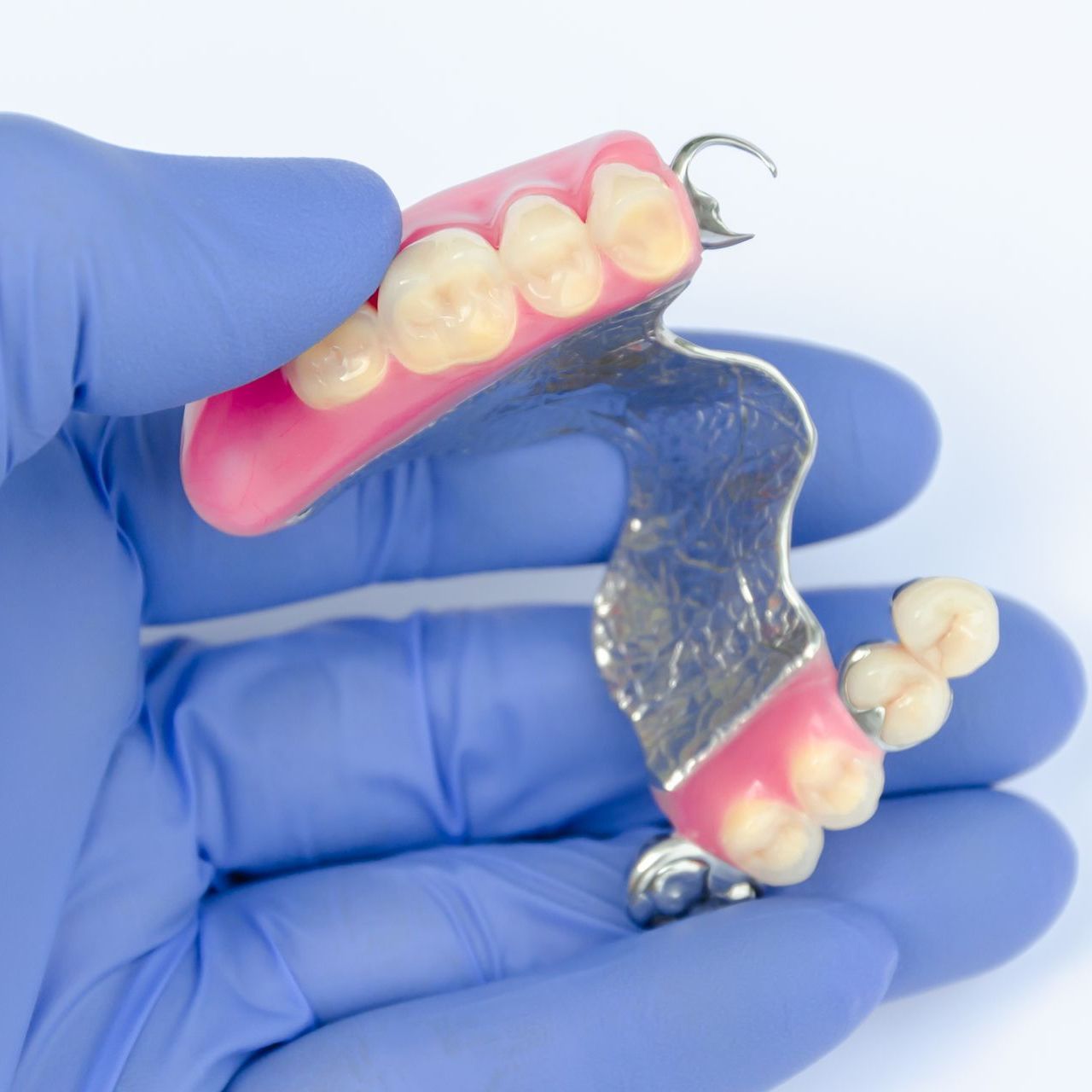 A person wearing blue gloves is holding a denture in their hand
