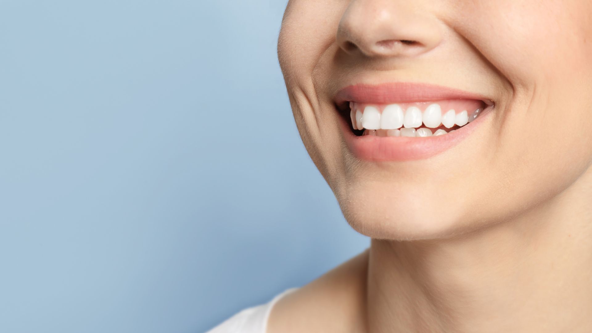 Un gros plan du sourire d'une femme avec des dents blanches sur fond bleu.