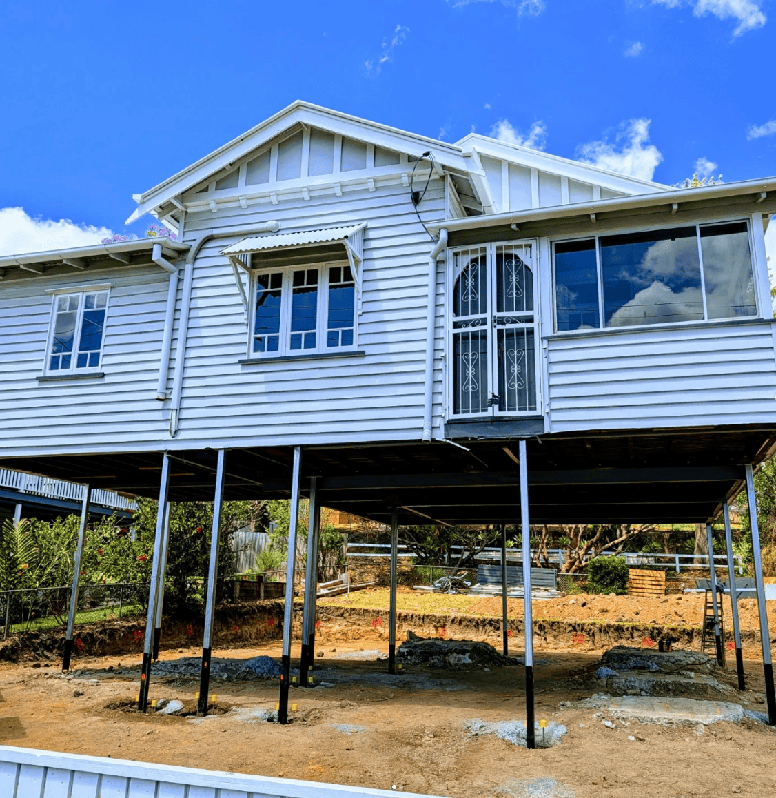 Elevated white wooden house on stilts with a front porch and blue sky overhead