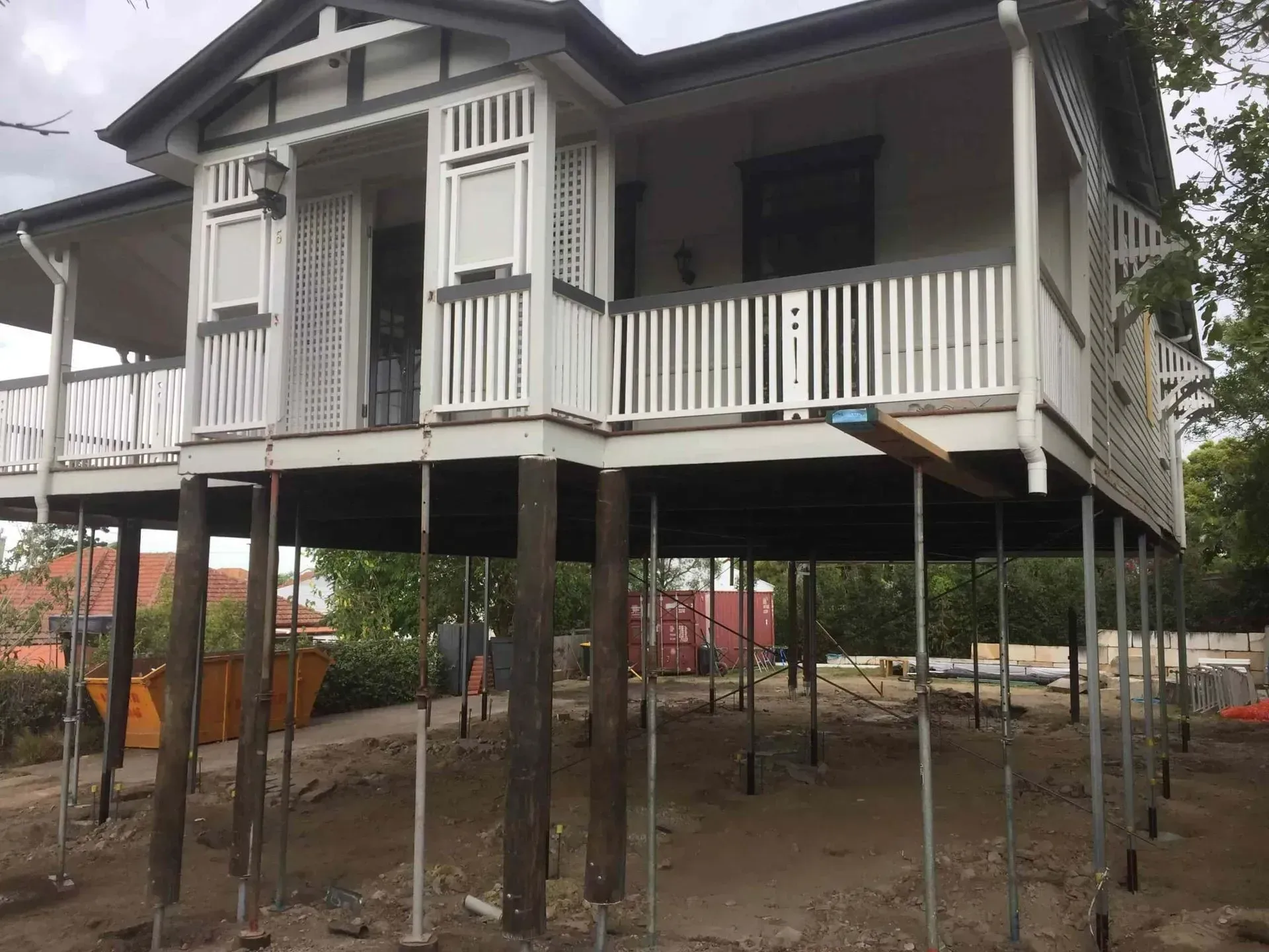 Elevated wooden house on stilts with white railings and shutters in a rural yard