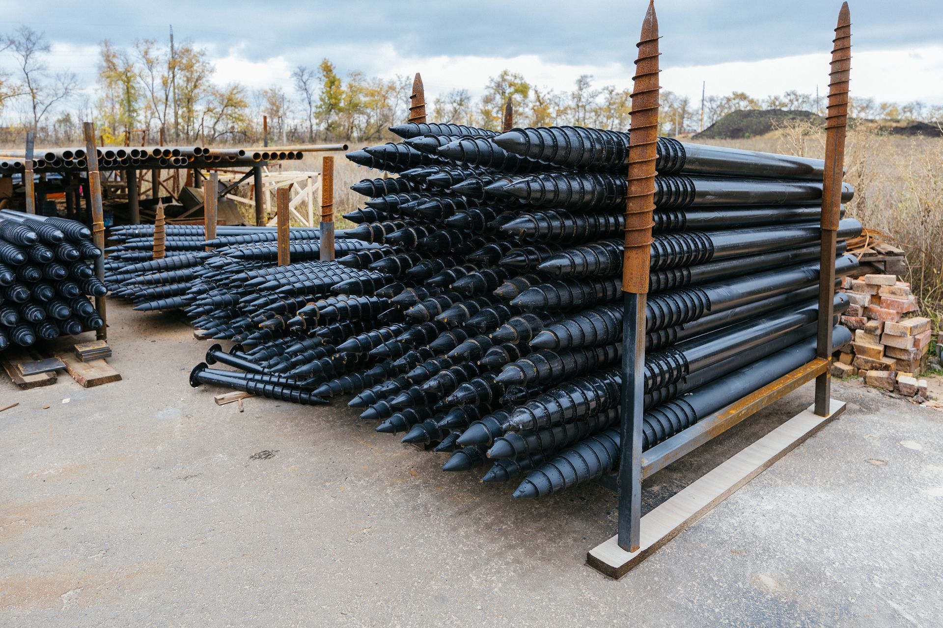 Stacks of black plastic pipes piled on a metal rack in an outdoor storage yard