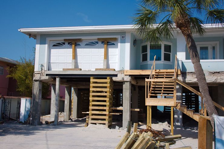 Partially built two-story house with exterior stairs, white walls, and palm trees in front