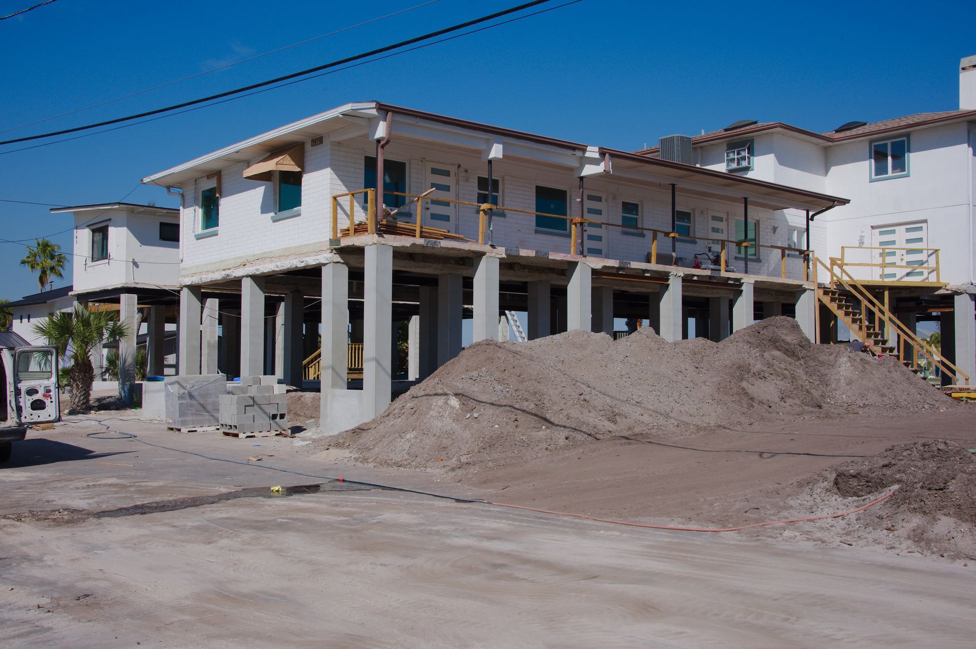 Partially built two-story house with exposed concrete, piles of dirt, and construction materials under a blue sky