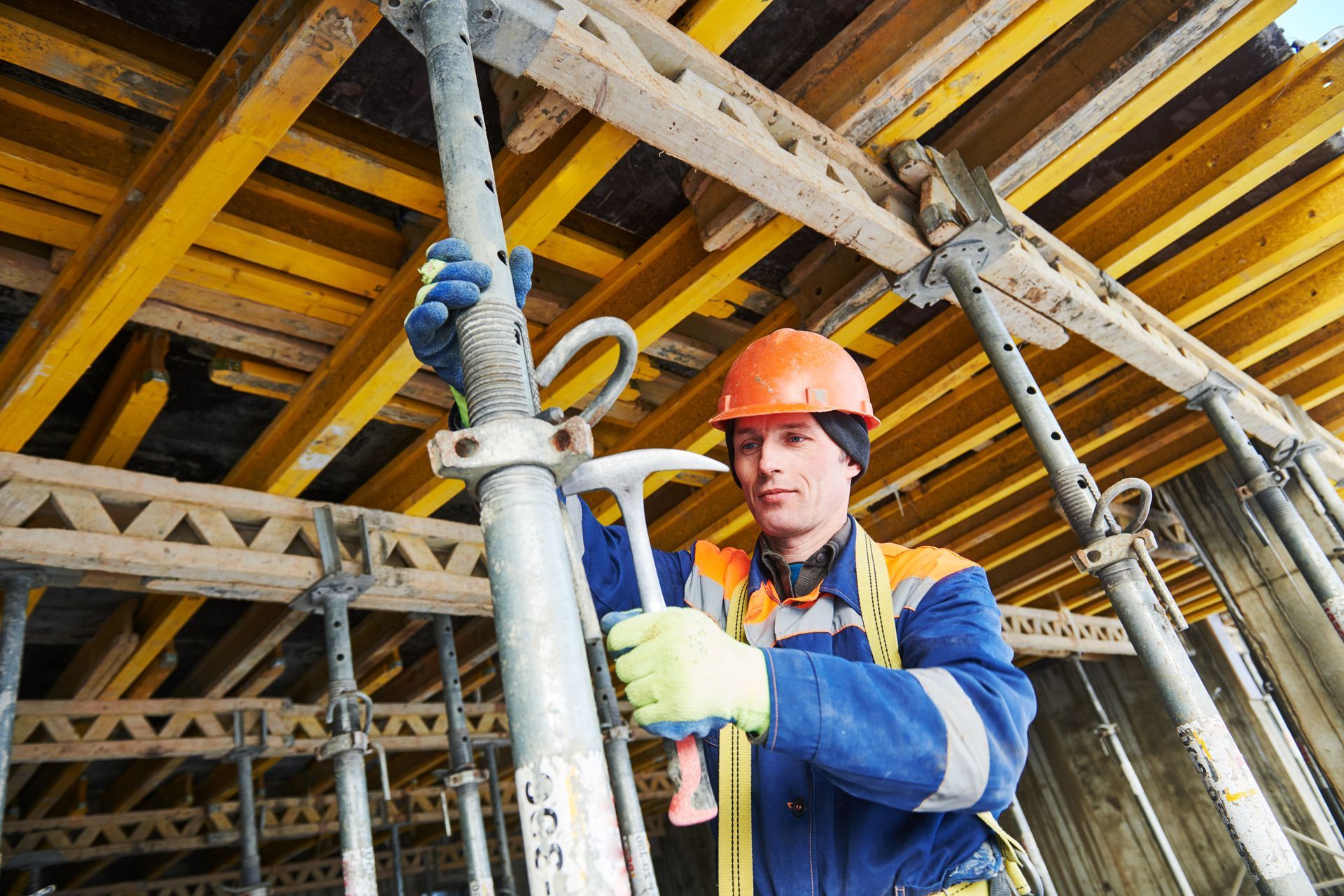 Construction worker in blue uniform and orange hard hat adjusting scaffolding indoors
