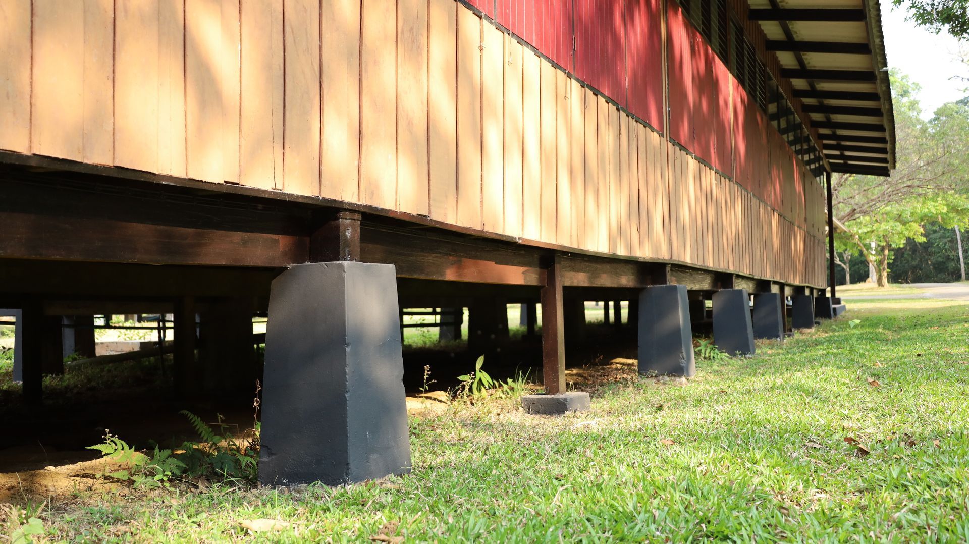 Wooden building on stilts with black supports, viewed from the side over grassy ground.