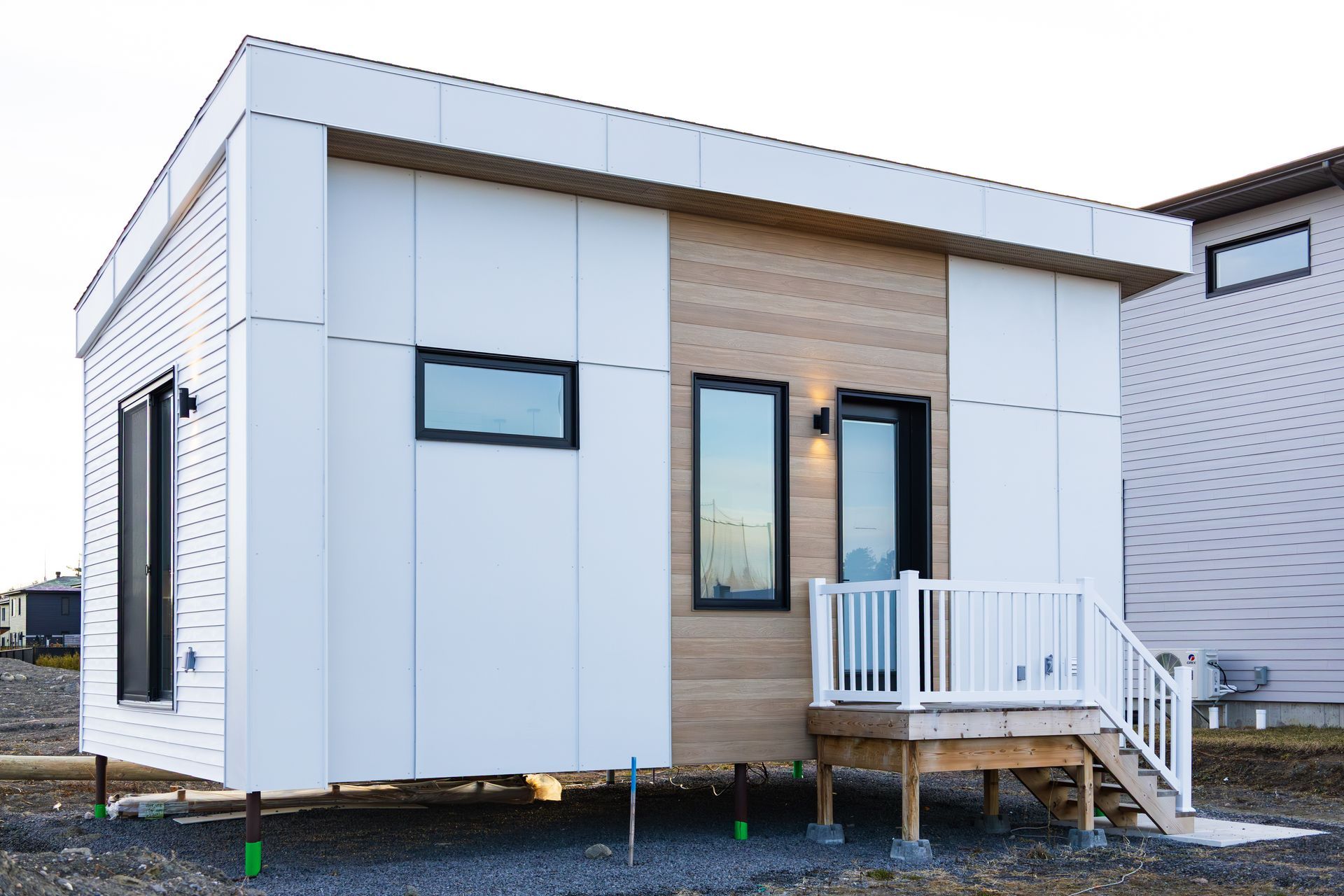 Small modern house with white and wood siding, a front porch, and steps on a gravel lot.