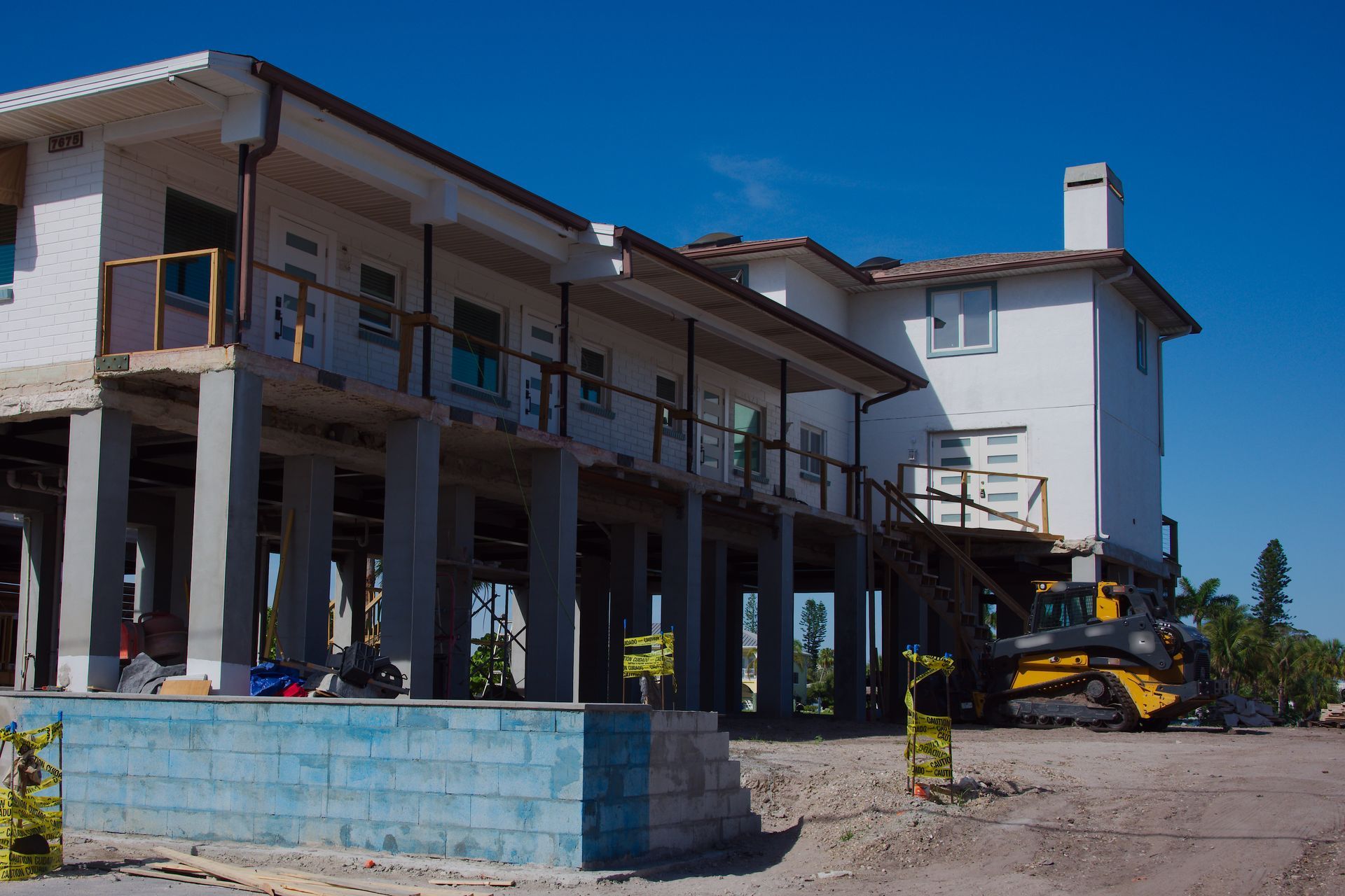 Partially renovated building with columns and a yellow excavator under a clear blue sky