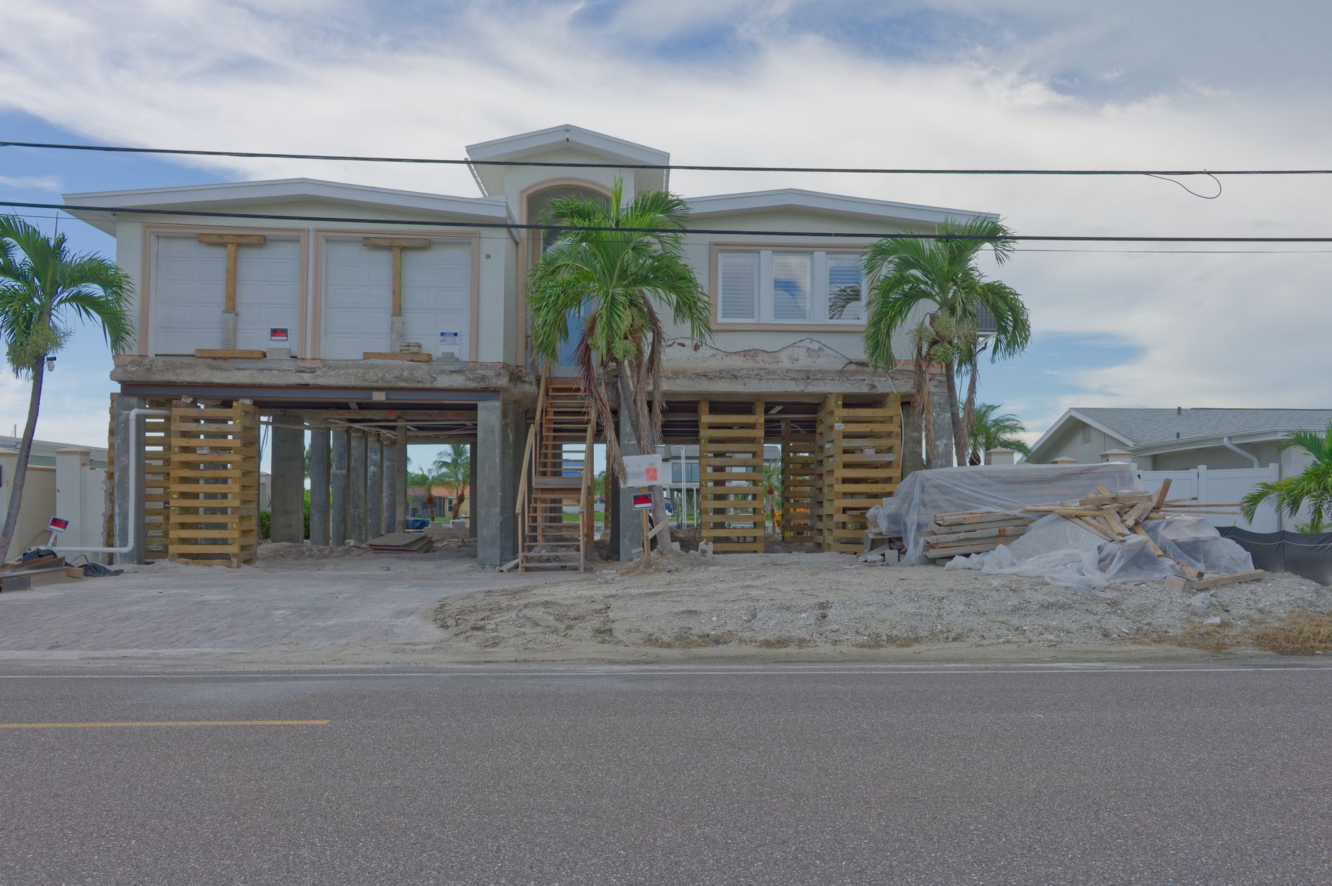 Raised beach house under construction with wooden framing and a coastal road in front