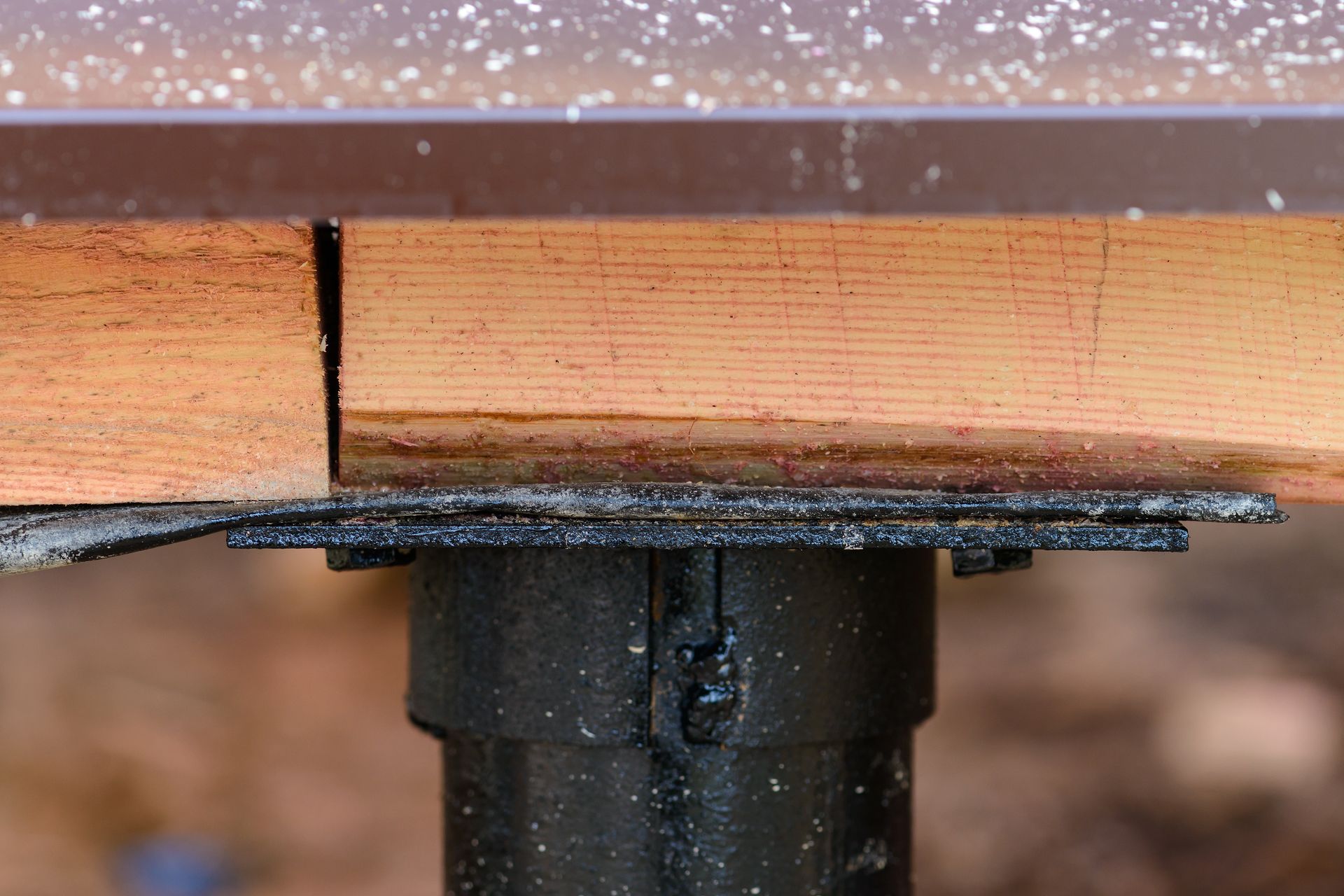 Close-up of a wooden beam mounted on a black metal post bracket outdoors.
