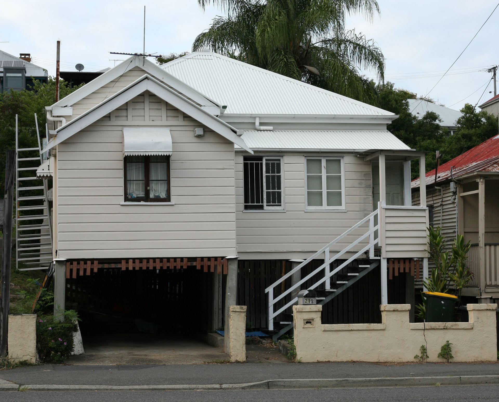 Small beige elevated house with white roof, front stairs, and carport under the main floor