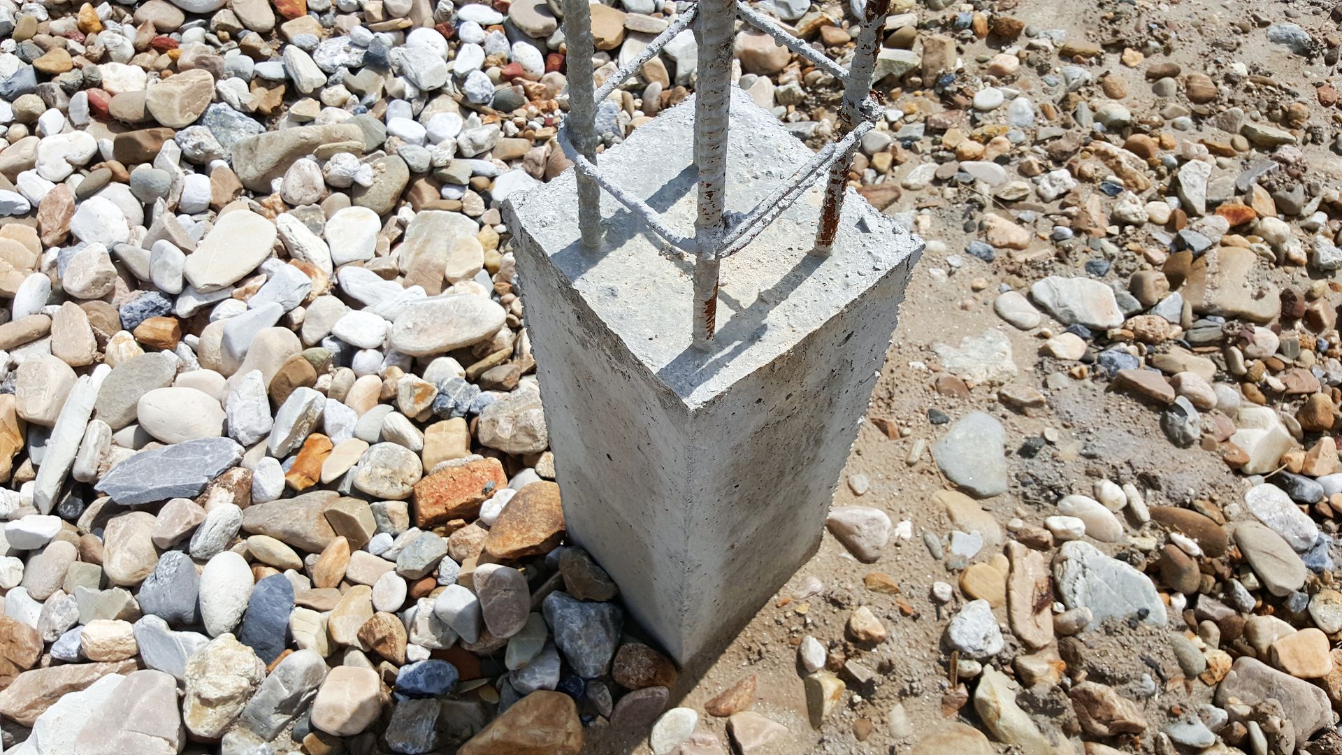 Concrete post base with exposed rebar on a gravel surface