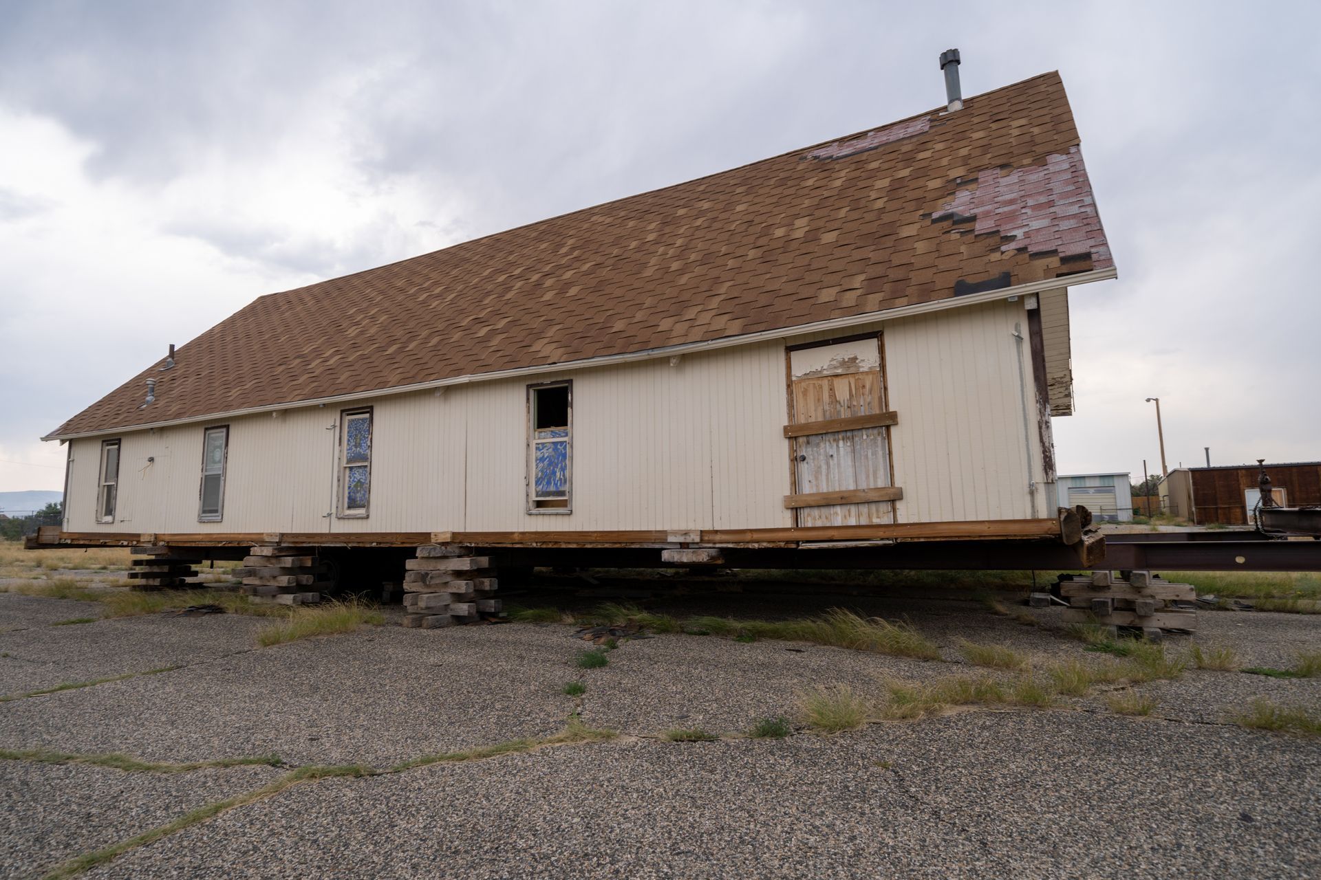 Old wooden building with a steep roof on a gravel lot under cloudy skies