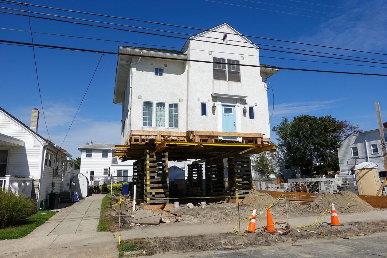 Raised white house under renovation on stilts, with construction cones and debris in front.