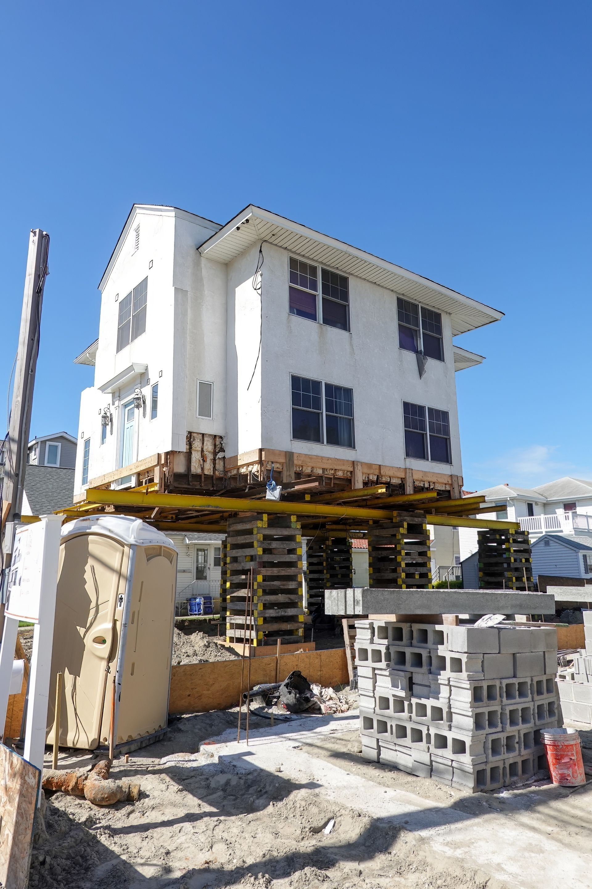 Partially built three-story white house with scaffolding and cinder blocks under a clear blue sky