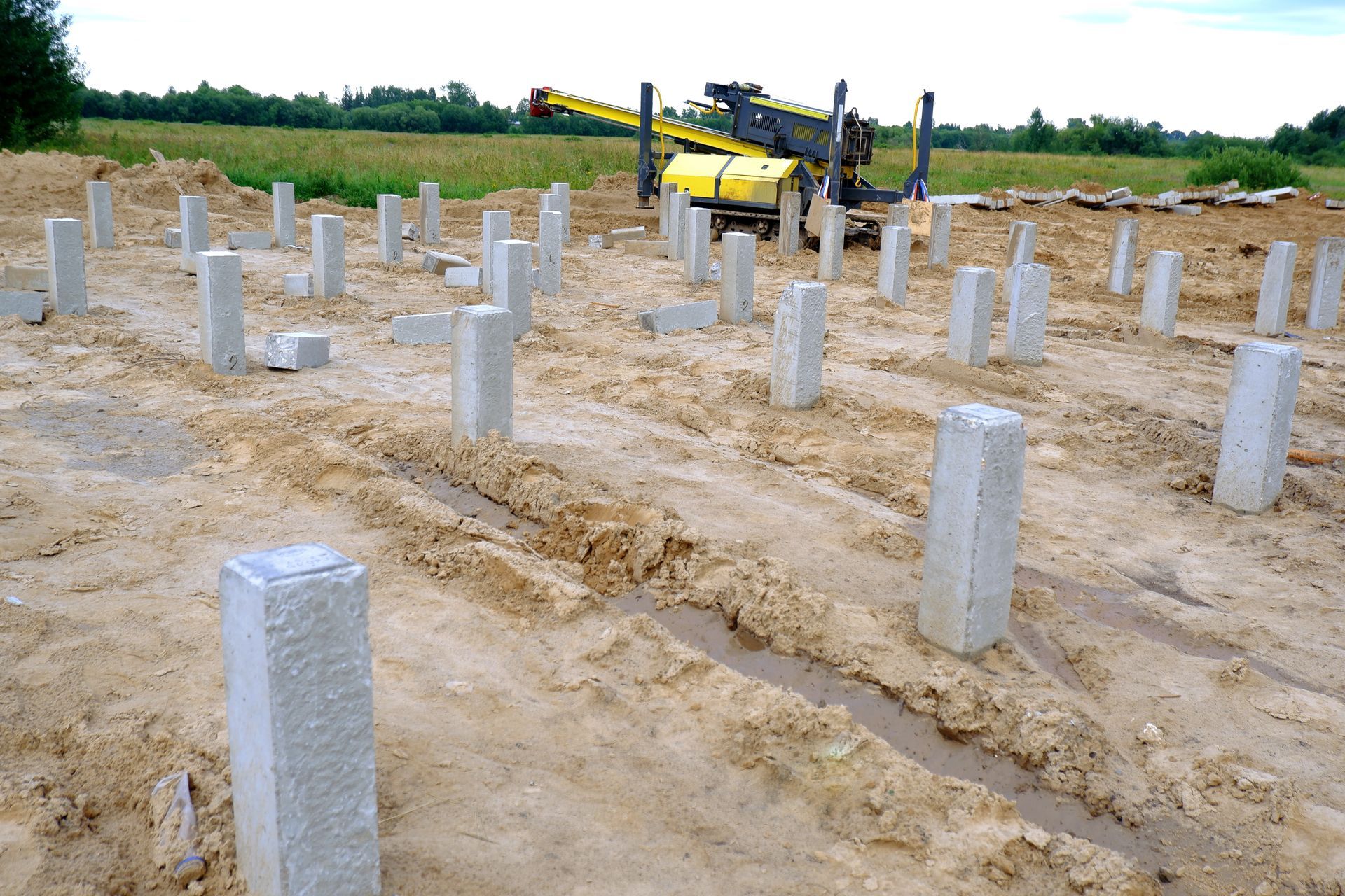 Concrete foundation piles on a construction site with a yellow drilling machine in the background