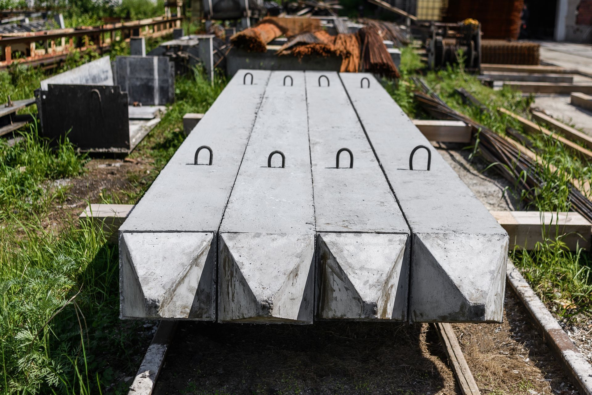 Large white concrete beams stacked outdoors on train tracks in a yard