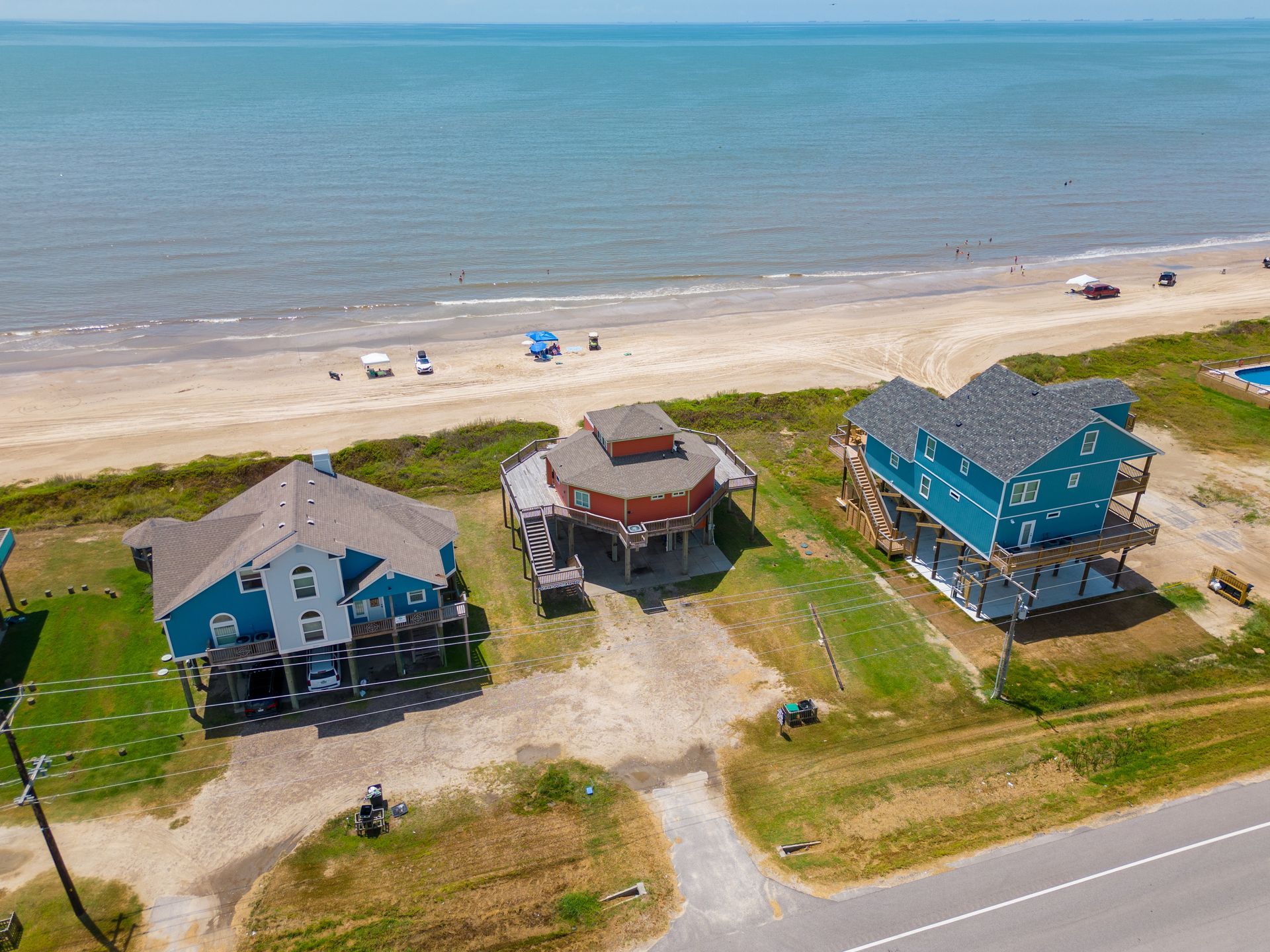 Aerial view of three beach houses beside a sandy shoreline and blue ocean.