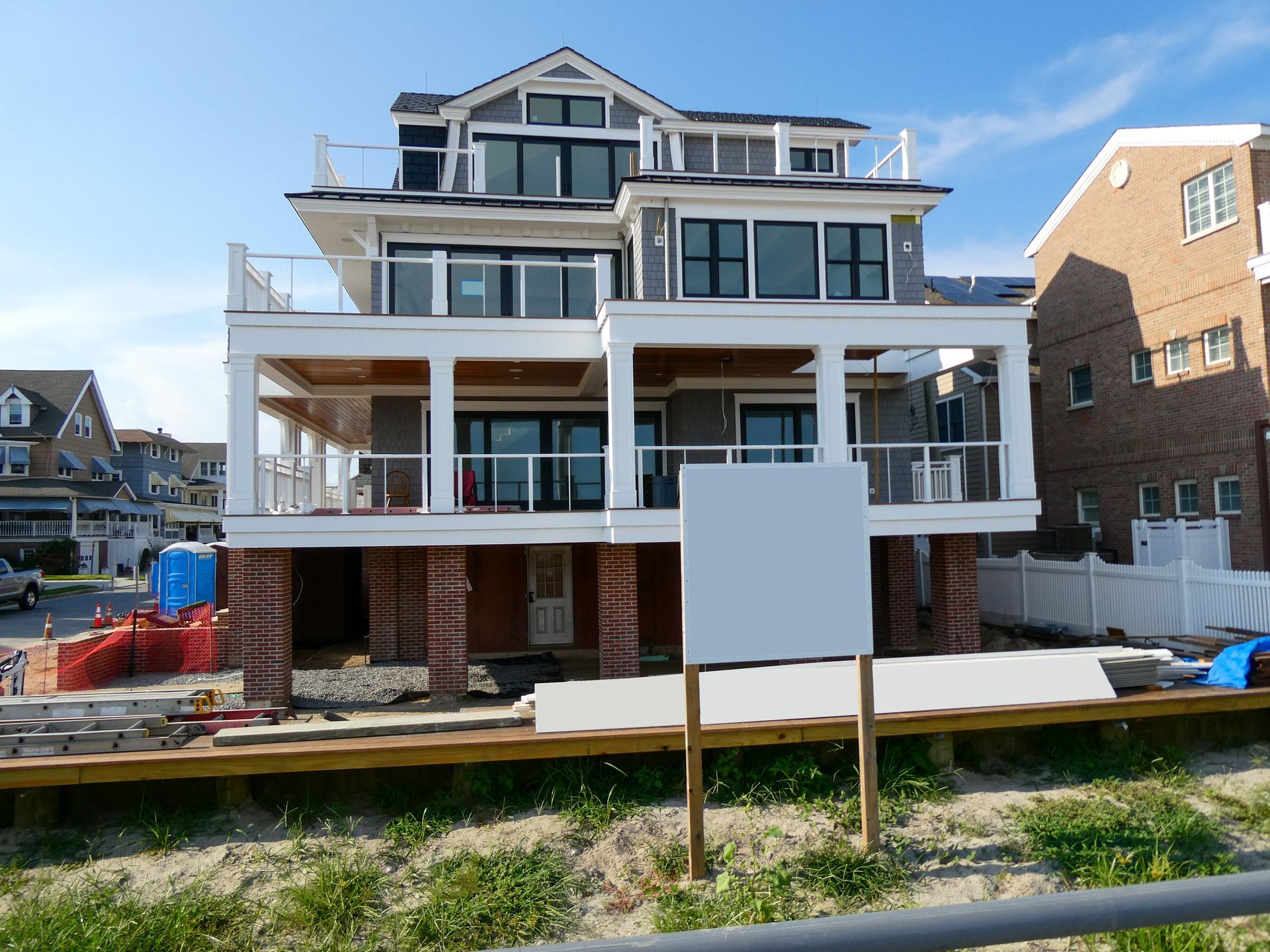 Large multi-story house under construction with white siding, porches, and a fenced front yard