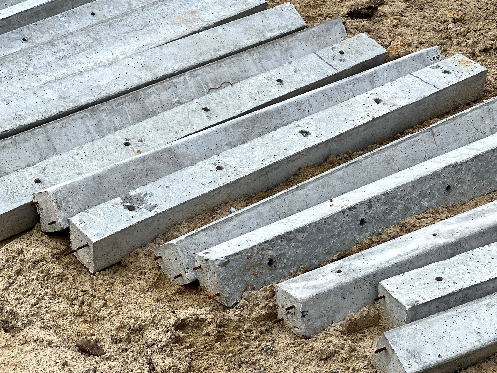 Gray concrete beams stacked on sandy ground at a construction site