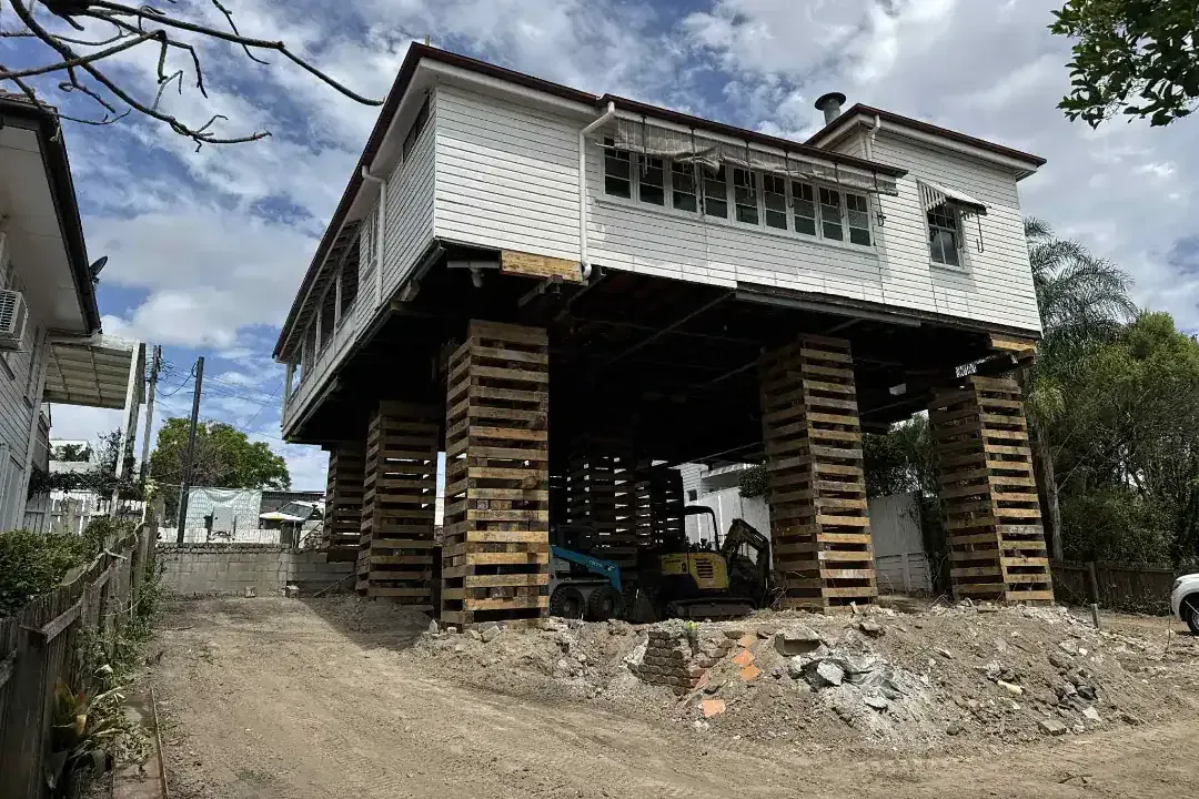 Raised house on wooden stilts at a construction site with debris and clouds overhead
